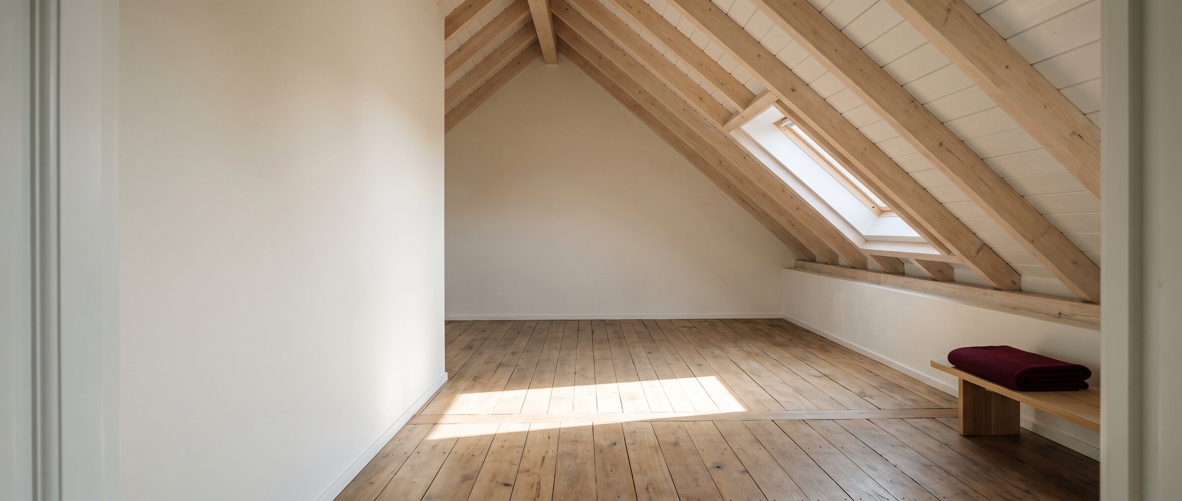 KI-generiertes Symbolbild: leeres Dachgeschoss mit Holzbalken, Dachfenster und Dielenboden im Morgenlicht