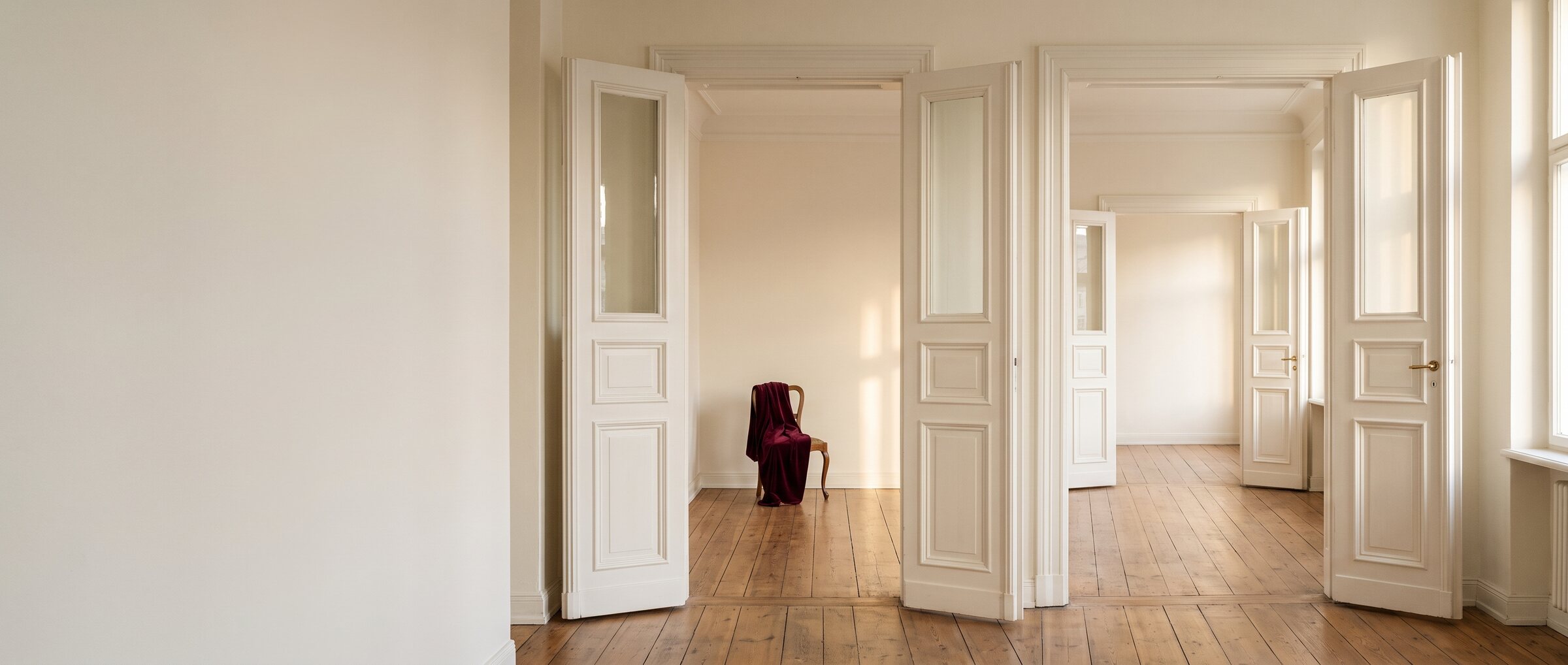 KI-generiertes Symbolbild: Blick durch drei leere Altbauzimmer mit offenen Fl&uuml;gelt&uuml;ren und Dielenboden