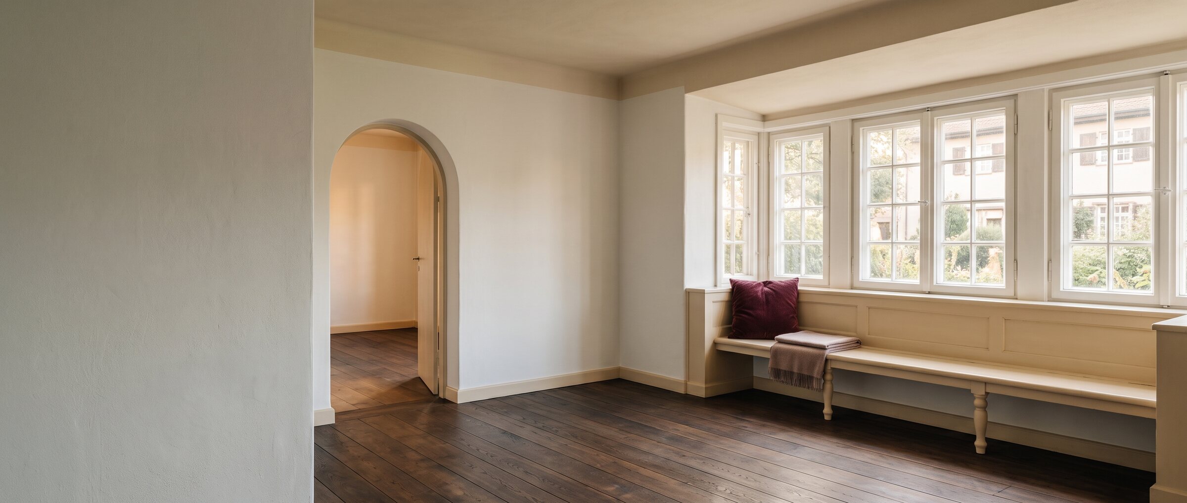 KI-generiertes Symbolbild: leeres Zimmer eines Siedlungshauses mit Sprossenfenstern, Fensterbank und Rundbogen zum Nachbarraum